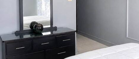 A bedroom with a bed, a dresser, a mirror, and a TV mounted on the wall.