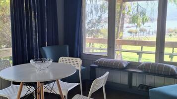 A covered outdoor seating area with a table and chairs, a bench with cushions, and a view of a lake and greenery.