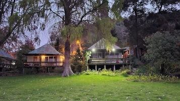 Una propiedad residencial con jardín, dos casas con terrazas de madera y un árbol grande al frente.
