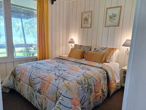 A bedroom with a bed, two bedside lamps, a window with curtains, and two framed pictures on the wall.
