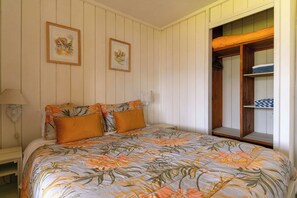 Un dormitorio con cama, dos cuadros en la pared, una mesita de noche y un armario de madera con ventana.