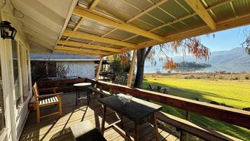 Une terrasse extérieure couverte, aménagée avec du mobilier en bois, offrant une vue sur un lac et un paysage montagneux en arrière-plan.