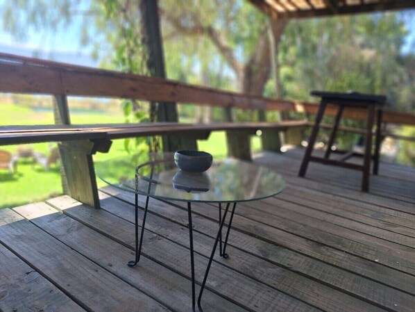 A glass-top table with a bowl on it, set on a wooden deck with a bench in the background.