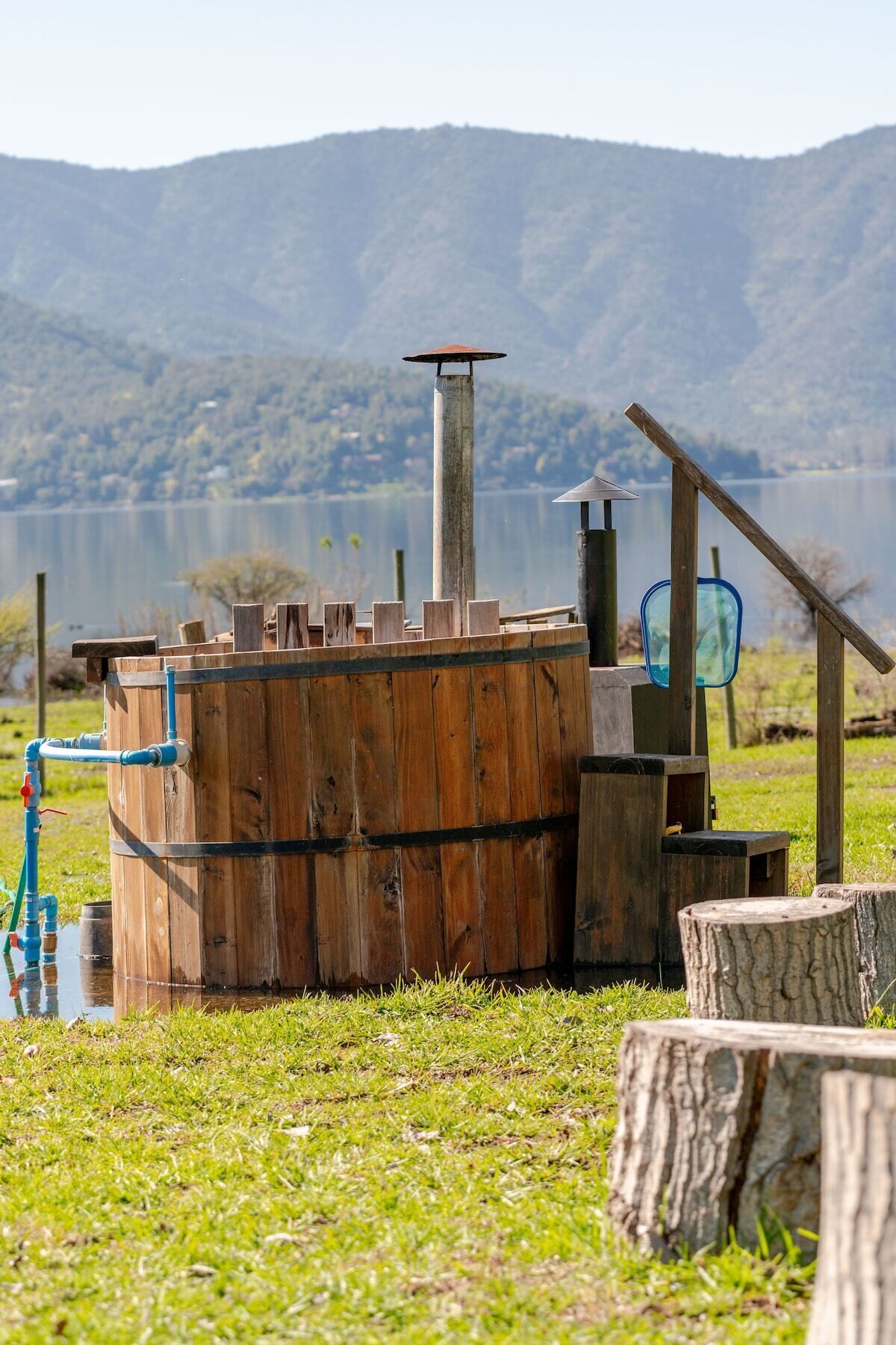 Un système de pompe à eau rustique installé à l’extérieur, comprenant un tonneau en bois, une structure métallique et une clôture en bois.