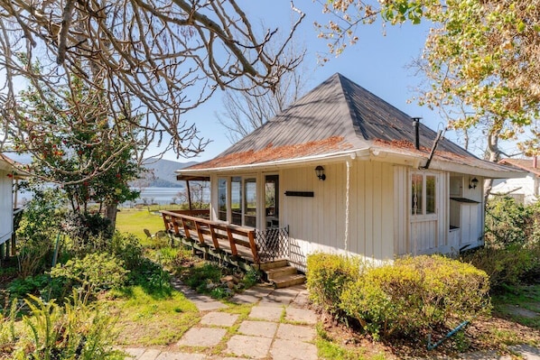 A white building with a porch, a wooden bench, and a stone pathway leading to the entrance.