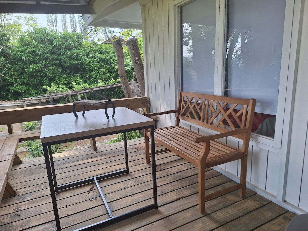 Una terraza de madera con mesa y banco, rodeada de follaje.