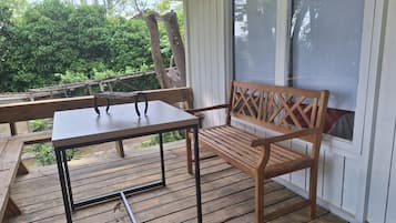 Una terraza de madera con mesa y banco, rodeada de follaje.