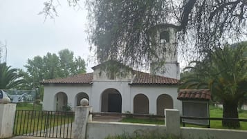 Un edificio blanco con techo de tejas y arcos, rodeado de vegetación.