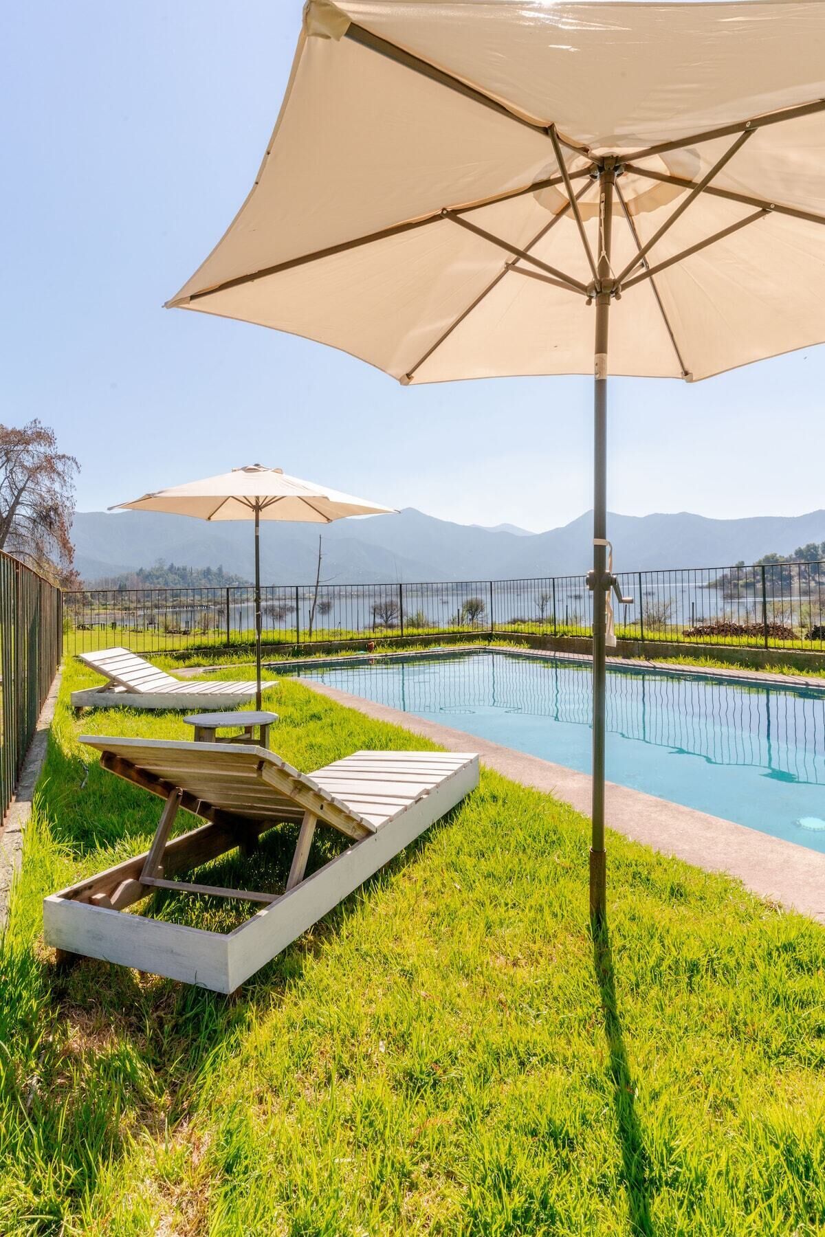 Un espace aménagé au bord de la piscine, avec des chaises longues et des parasols, entouré d’une clôture et offrant une vue sur les montagnes lointaines.