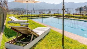 Un espace aménagé au bord de la piscine, avec des chaises longues et des parasols, entouré d’une clôture et offrant une vue sur les montagnes lointaines.