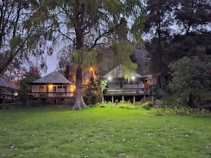 A residential property with a large lawn, a house with a deck, and a tree in the foreground.