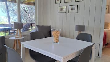 Un comedor con una mesa blanca, sillas negras y un florero de vidrio transparente con una planta.