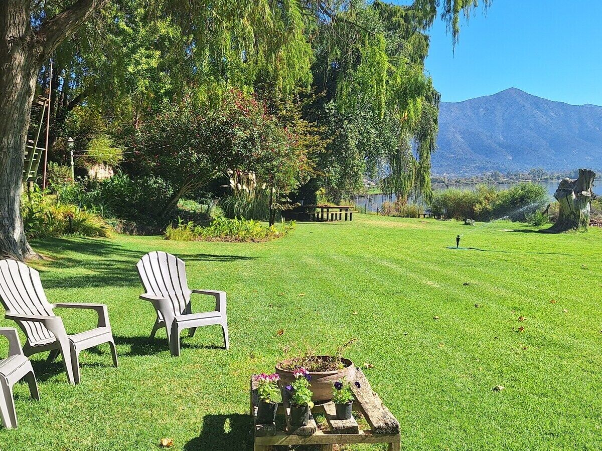Un espace extérieur verdoyant, avec des fauteuils Adirondack, une table en bois agrémentée de plantes en pot et une montagne en arrière-plan.