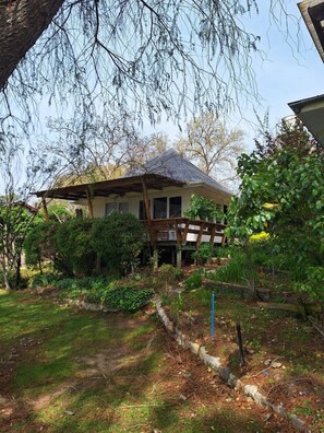 Uma casa com varanda, cercada por um jardim com diversas plantas e um pequeno lago.