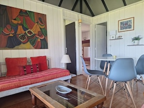 Quarto com cama, mesa e cadeira. Há um quadro na parede e um porta-retrato.