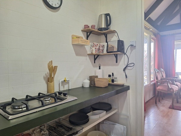 A kitchen with a gas stove, shelves with kitchenware, and a coffee maker.