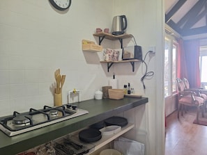 A kitchen with a gas stove, shelves with kitchenware, and a coffee maker.