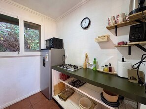 A compact kitchen with a refrigerator, microwave, gas stove, and a clock on the wall.