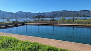 A rectangular pool with a clear blue water surface, surrounded by a metal fence, and a view of mountains and a lake in the background. - Lakefront Cabin: Hot Tub, Pets OK, Near Santiago (Maipo)