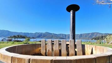 Una estructura de barriles de madera con un poste central, rodeada por una plataforma circular de madera, frente a un paisaje de montañas y cielo despejado.