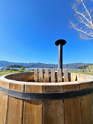 Une structure en forme de tonneau, faite de bois, avec un poteau central, entourée d’une plateforme circulaire également en bois, le tout se dressant sur un fond de montagnes et d’un ciel dégagé.