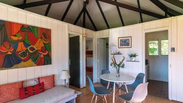 A room with a white ceiling, a colorful abstract painting, a sofa with red cushions, a round table with chairs, and a door leading to another room.