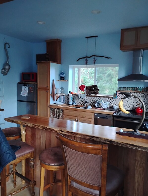 A kitchen with a bar area, wooden cabinets, and a window providing a view of greenery. - Top of the world lookout cabin, with a 360% view, Olympic Mountains to the sea. (Port Angeles)