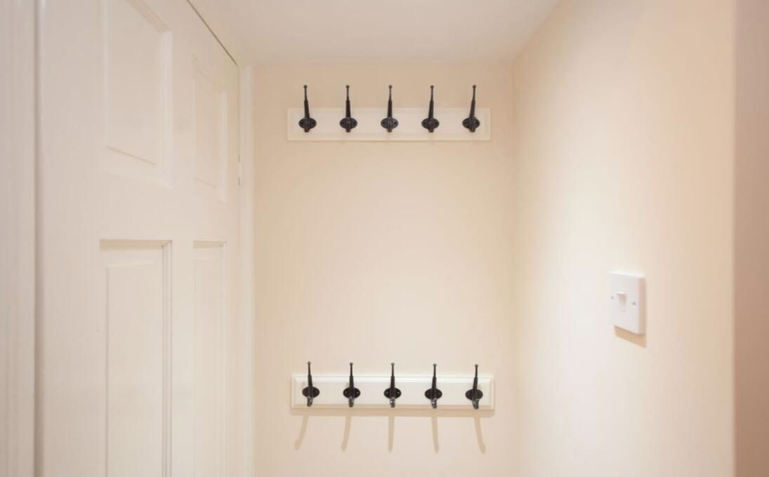 A hallway with two rows of black wall-mounted hooks on white walls.