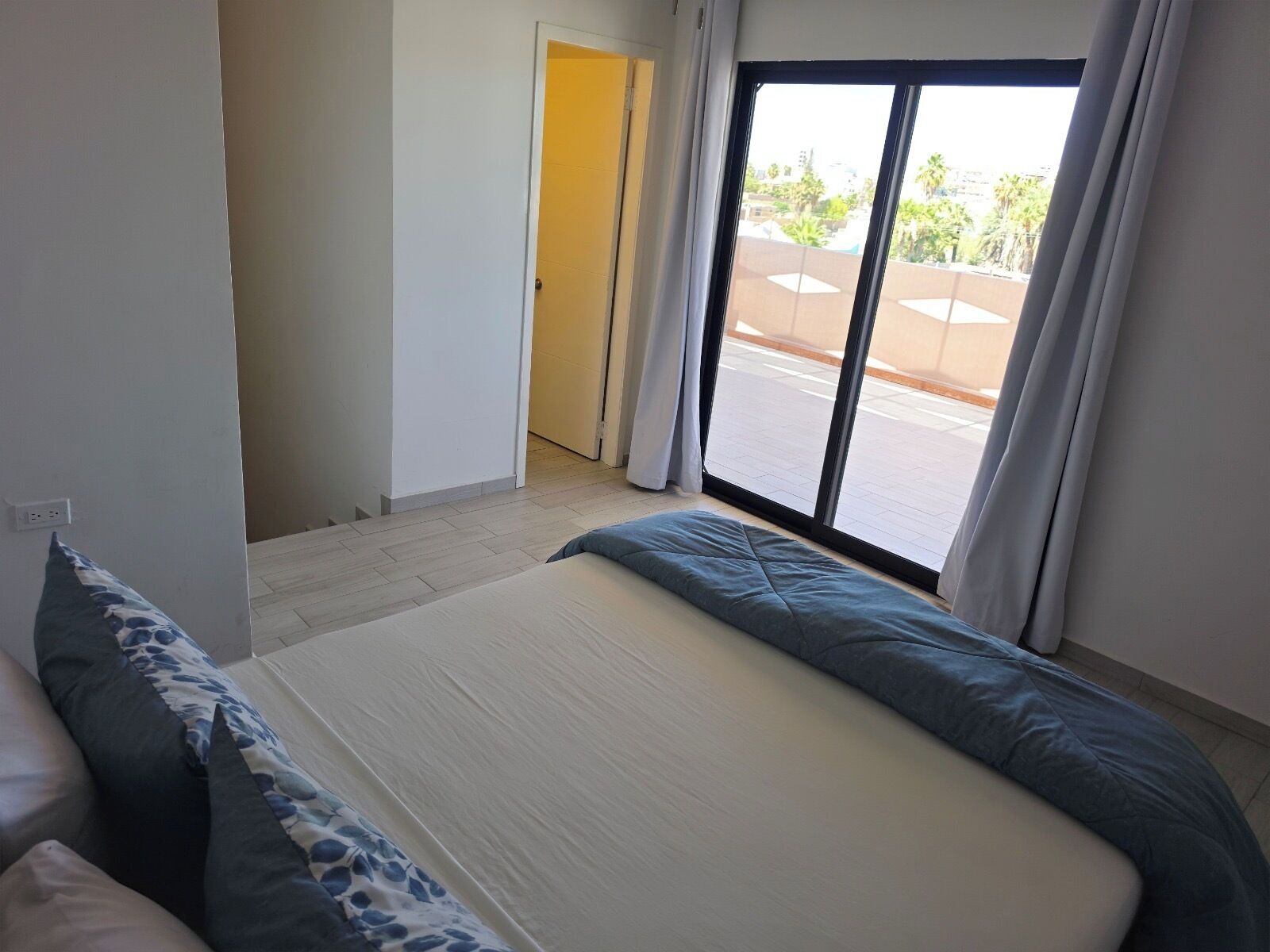 A bedroom with a bed, a window, and a door leading to a balcony.