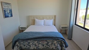 Un dormitorio con una cama, dos mesitas de noche, una ventana y un cuadro en la pared.