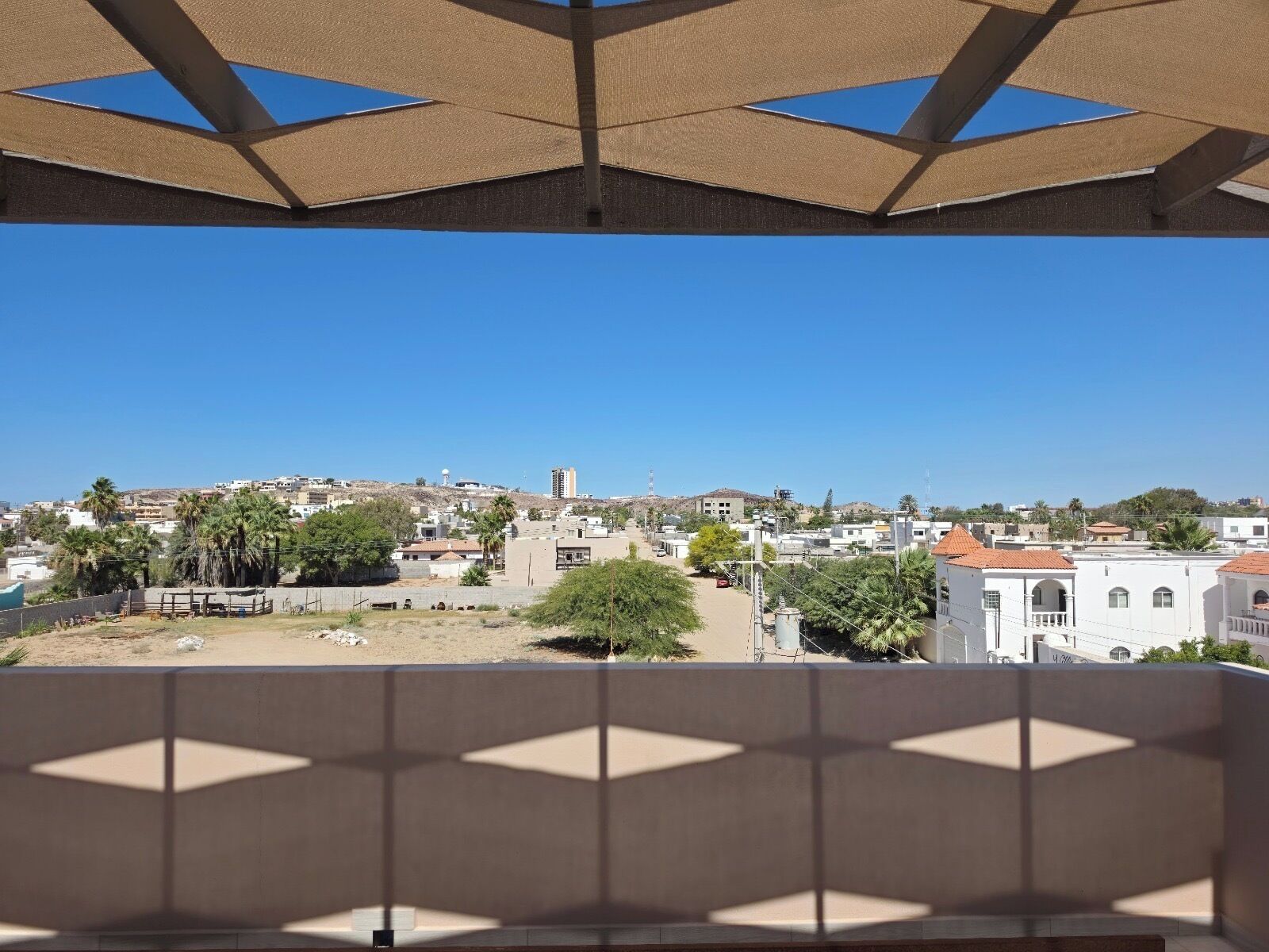 A balcony with a view of a residential area, including buildings and trees.