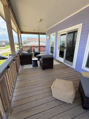 Eine überdachte Holzterrasse mit Sitzgelegenheit, Kissen und einem Tisch sowie eine Schiebetür aus Glas.