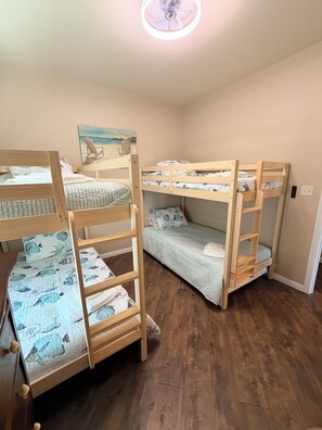 Ein Zimmer mit Etagenbetten, einem Strandbild und einem Deckenventilator.