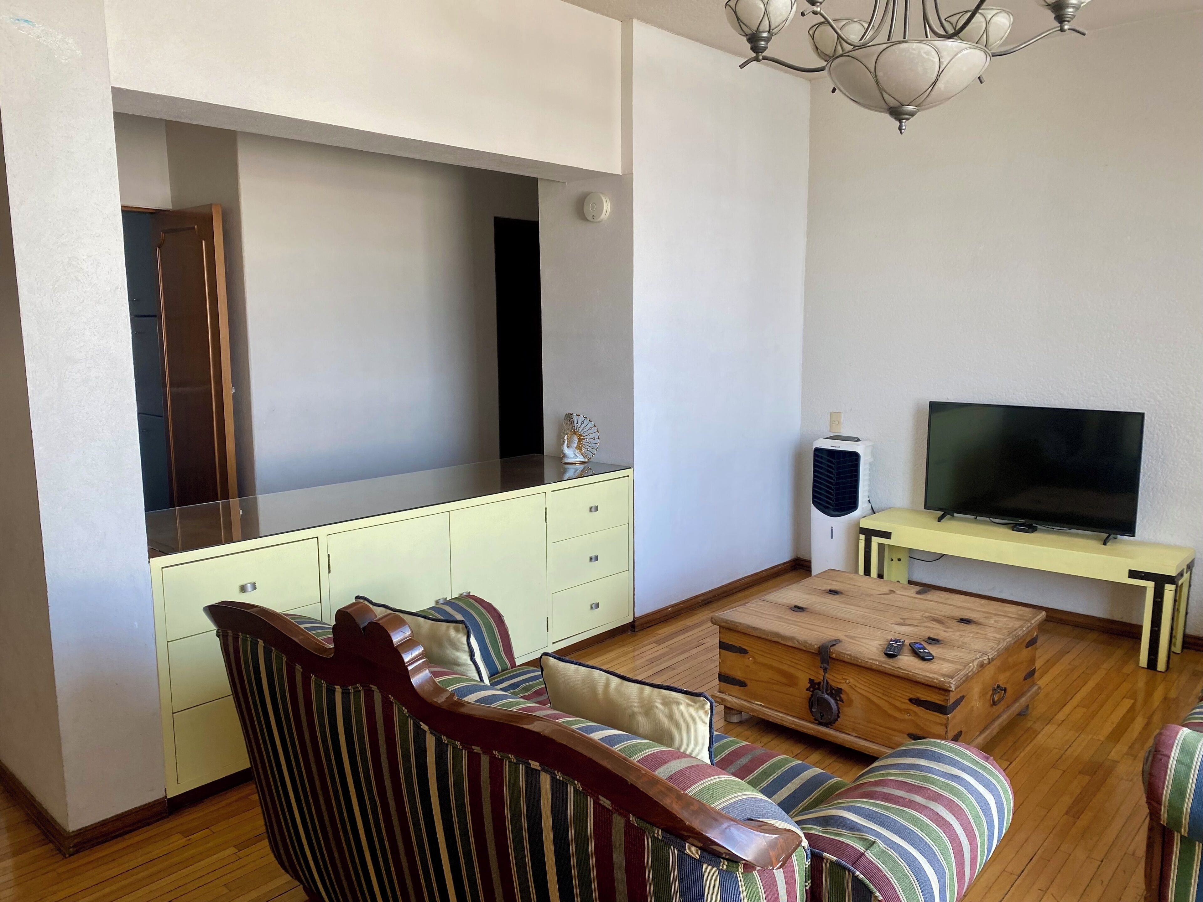 A living room with a sofa, a television on a stand, a cabinet, and a wooden chest.