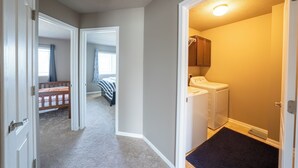 Un couloir mène à une chambre avec un berceau, un espace buanderie avec un lave-linge et un placard avec une tringle pour suspendre les vêtements.