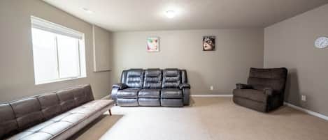 Un salon avec un tapis beige, un canapé marron foncé, un fauteuil inclinable et un banc.