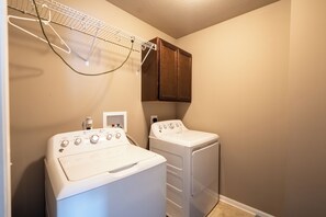 A laundry room with two white washing machines, a drying rack, and a wooden cabinet. - Your Home Away from Home (Omaha)