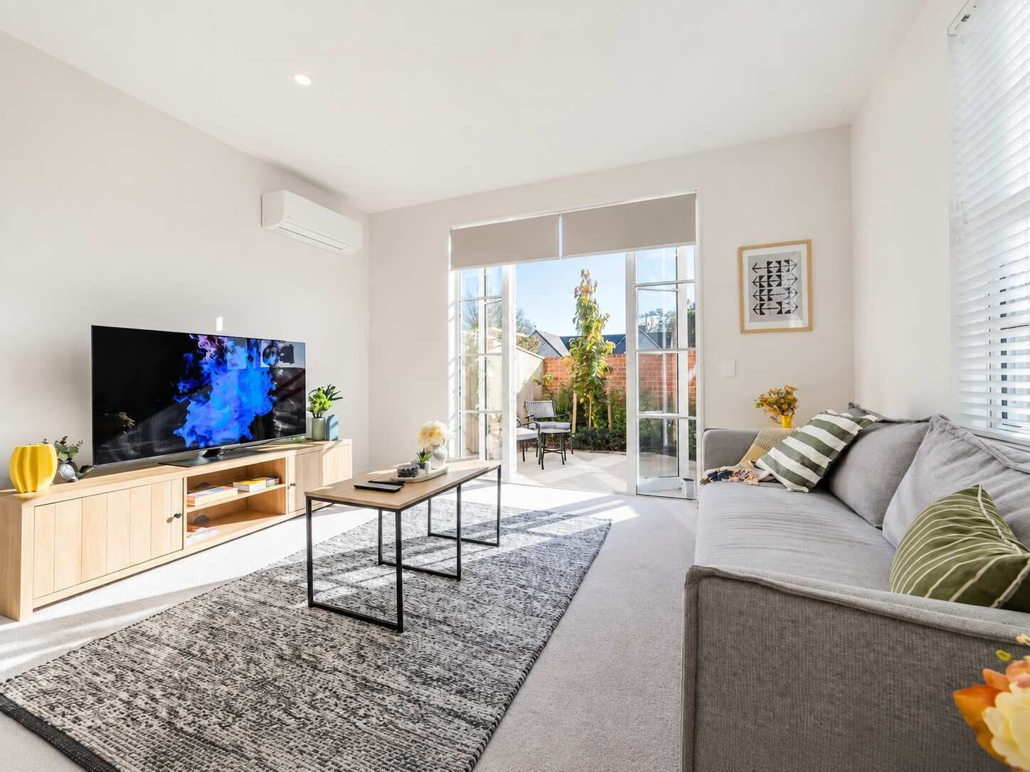 A modern living room with a flat-screen TV, a sofa, a coffee table, and a patterned rug.