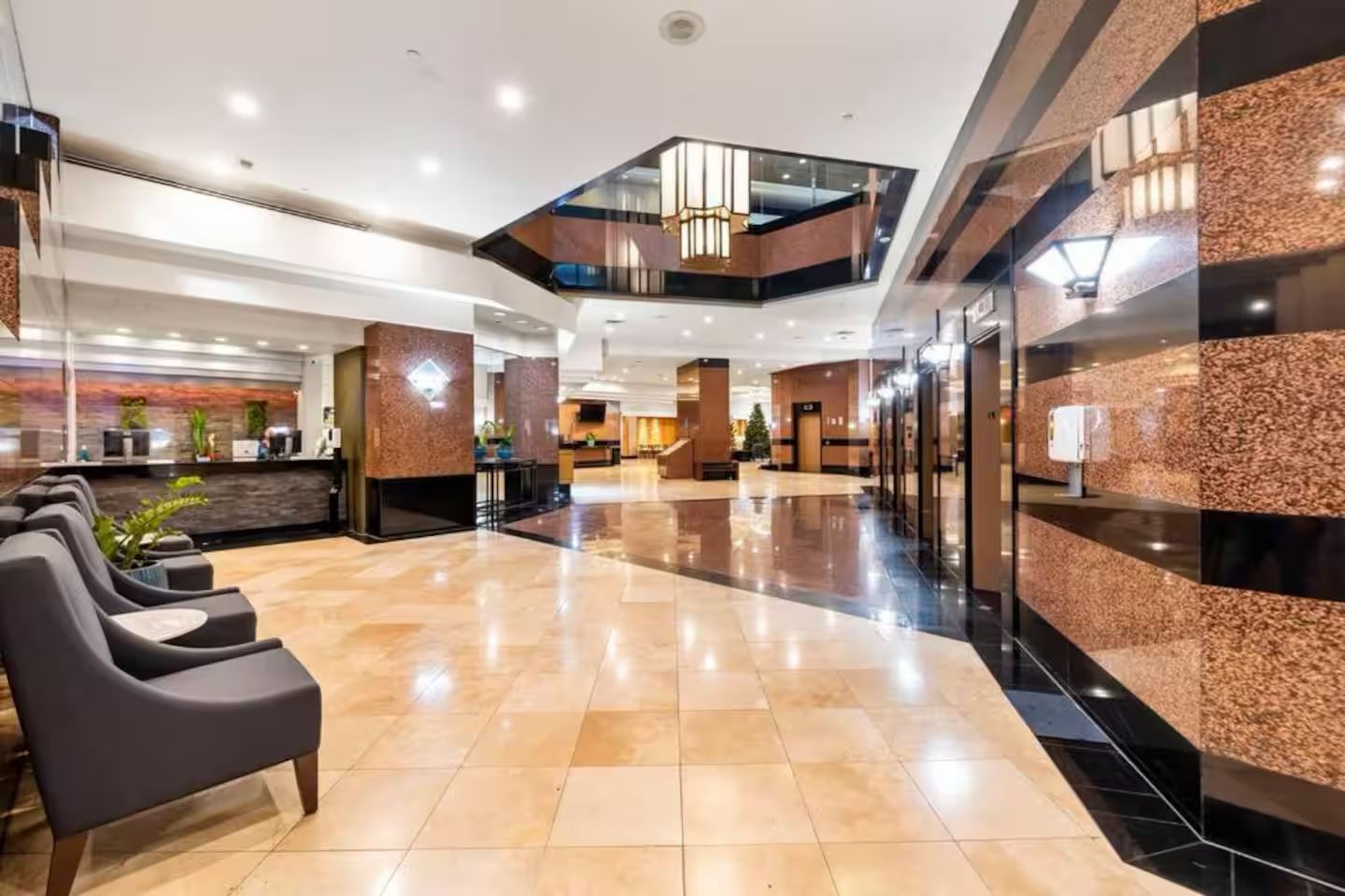 A hotel lobby with a reception desk, seating area, and a modern staircase.