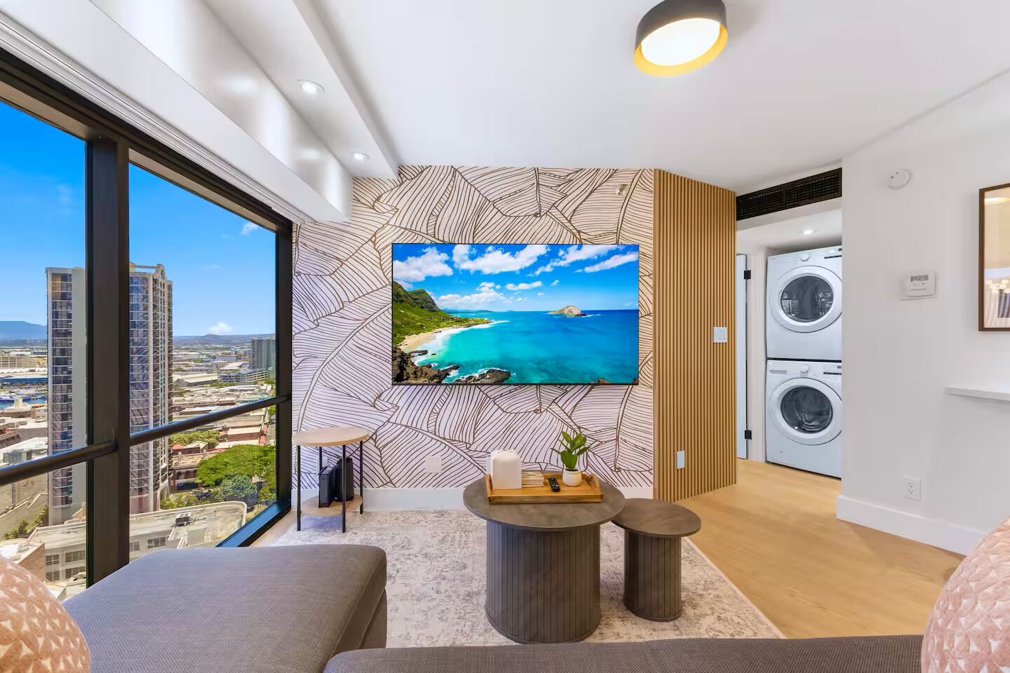 A modern living room with a large TV, a sofa, a small coffee table, and a view of the cityscape.