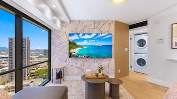 A modern living room with a large TV, a sofa, a small coffee table, and a view of the cityscape.