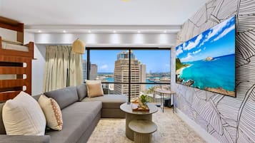 A modern living room with a sofa, a coffee table, and a large window offering a city view.