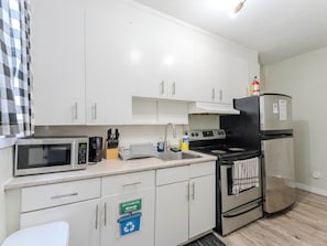 A compact kitchen with white cabinets, a microwave, a stove, and a refrigerator.