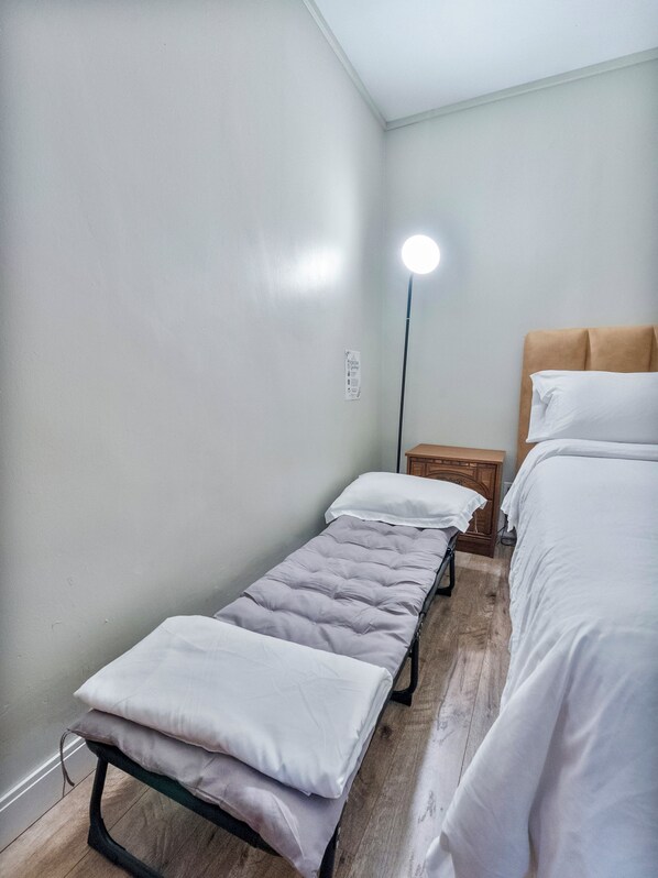 A small, single-room accommodation with a bed, a bench, and a bedside table.