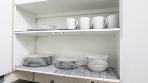 A white shelf with stacked white plates and bowls, and white cups and mugs.