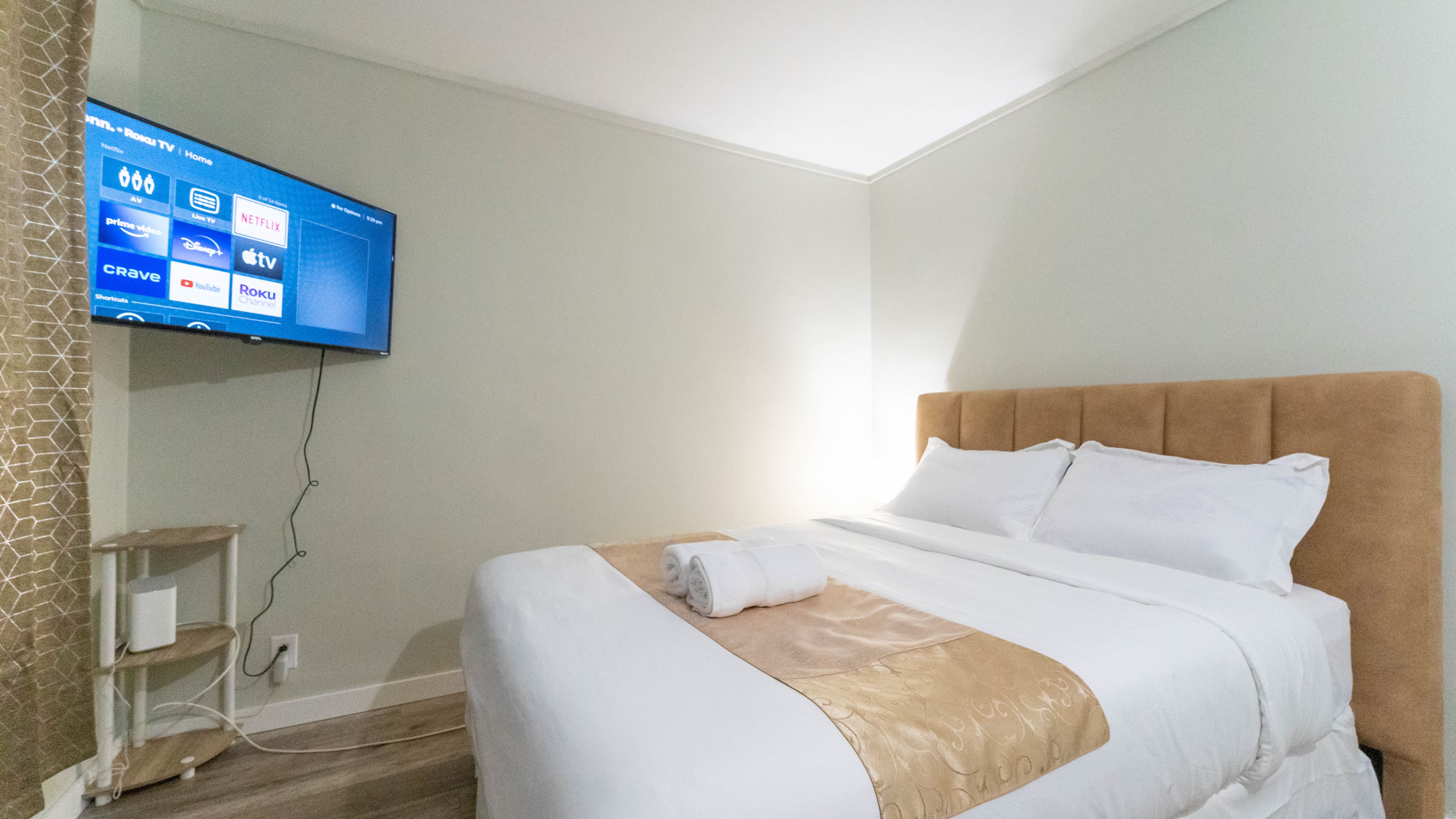 A hotel room with a bed, a television mounted on the wall, and a small bedside table.