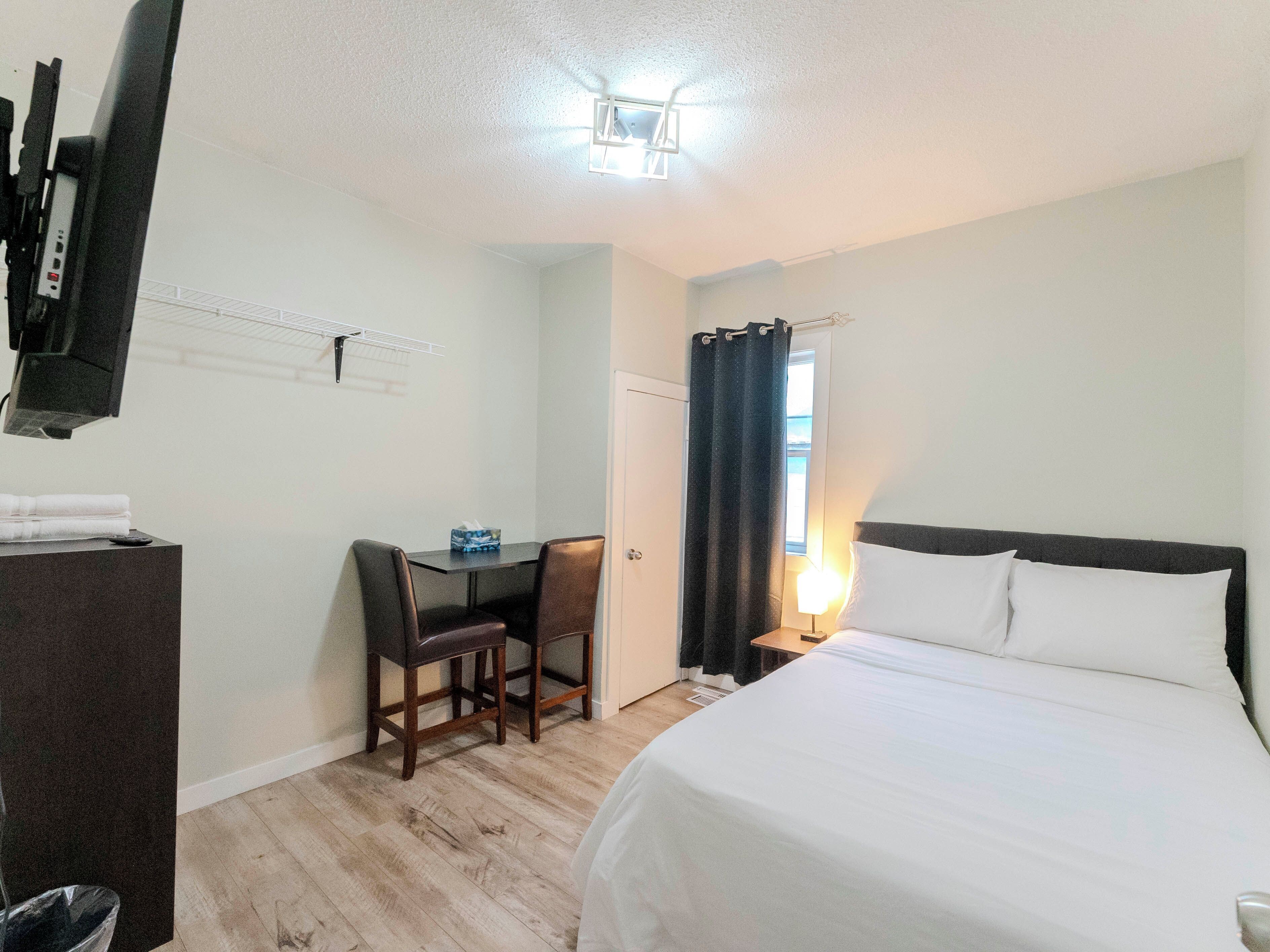 Une chambre d’hôtel avec un lit, un bureau et une chaise, une télévision et une fenêtre avec des rideaux.