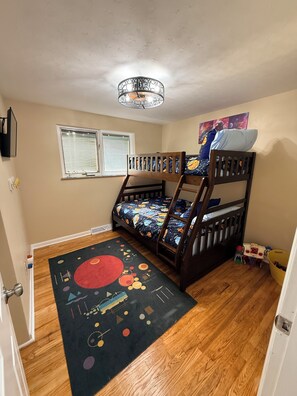 A child's bedroom with a bunk bed, a space-themed bedspread, a star-patterned rug, and a wall-mounted shelf.