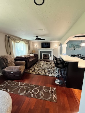A living room with a fireplace, a sofa, a coffee table, and a dining area with bar stools.