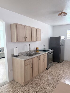 A kitchen with wooden cabinets, a stainless steel sink, a stove, and a refrigerator. - Caribe Social House-Stay • Celebrate • Connect (Loiza)